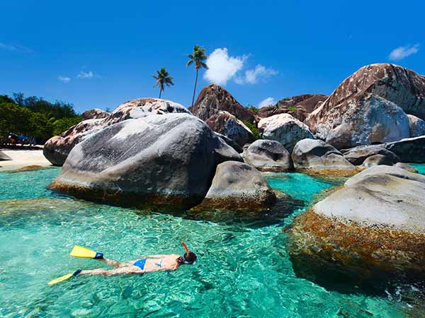 Young woman snorkeling in turquoise tropical water among huge granite boulders at The Baths beach area major tourist attraction on Virgin Gorda, British Virgin Islands, Caribbean